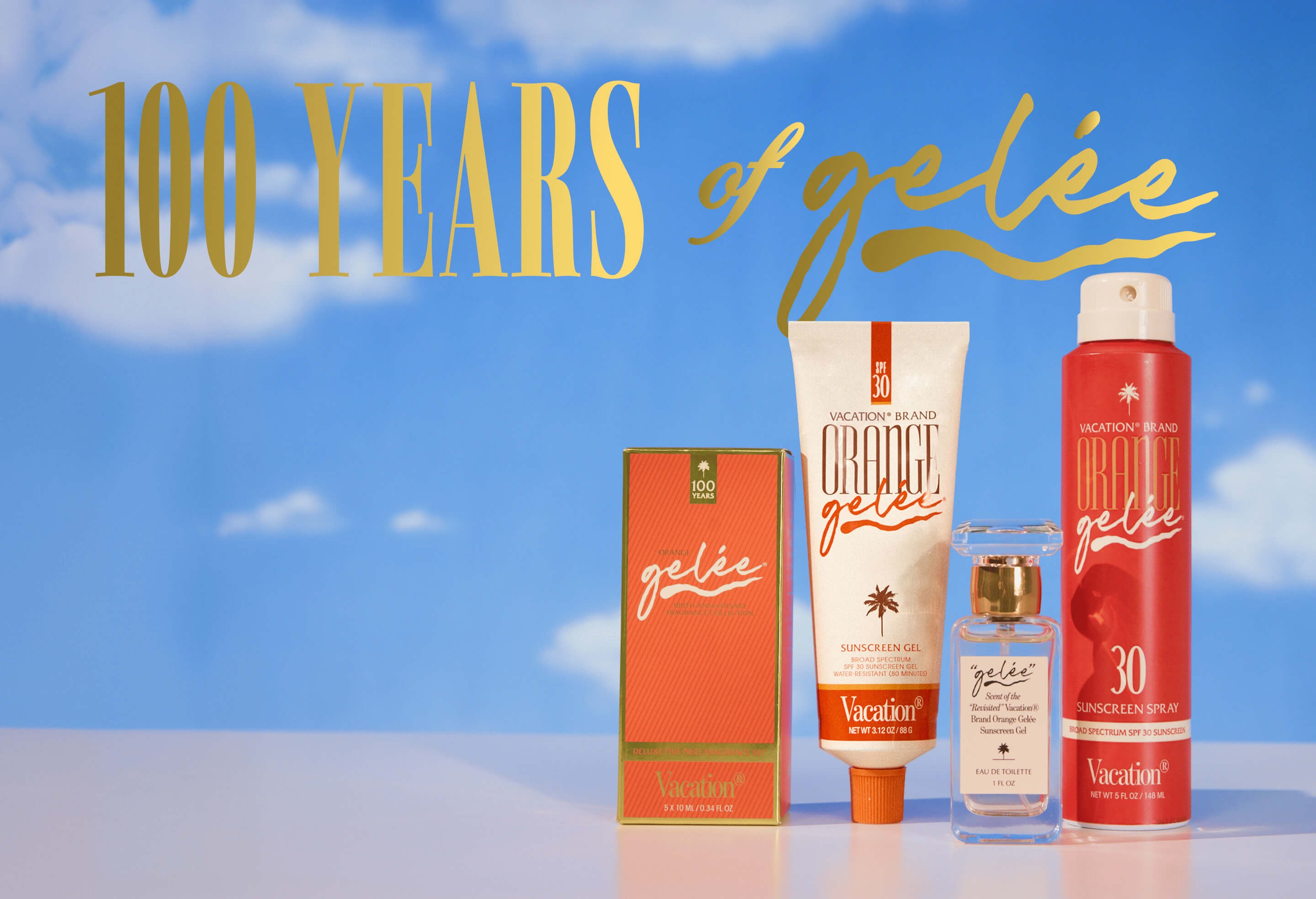 A collection of Vacation brand Orange Gêlée sunscreens and fragrance products against a blue sky with clouds.