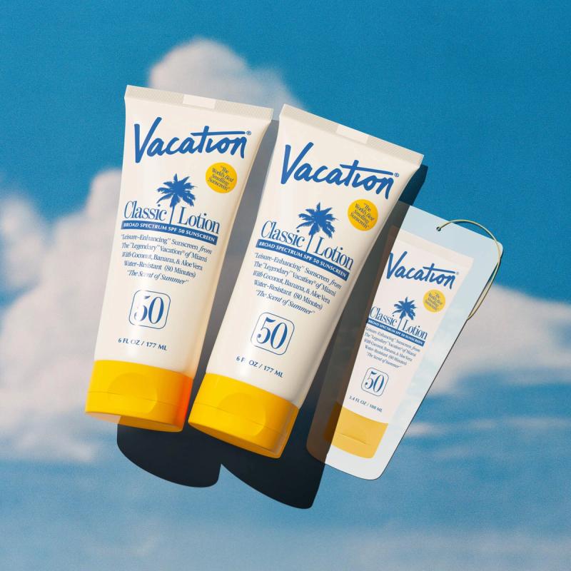 Two Vacation Classic Lotion SPF 50 sunscreen tubes and a small product tag against a blue sky with clouds.