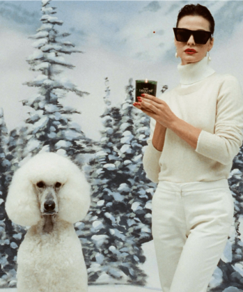 a woman in a white sweater holds a Royal Pine Deluxe candle standing next to a white poodle