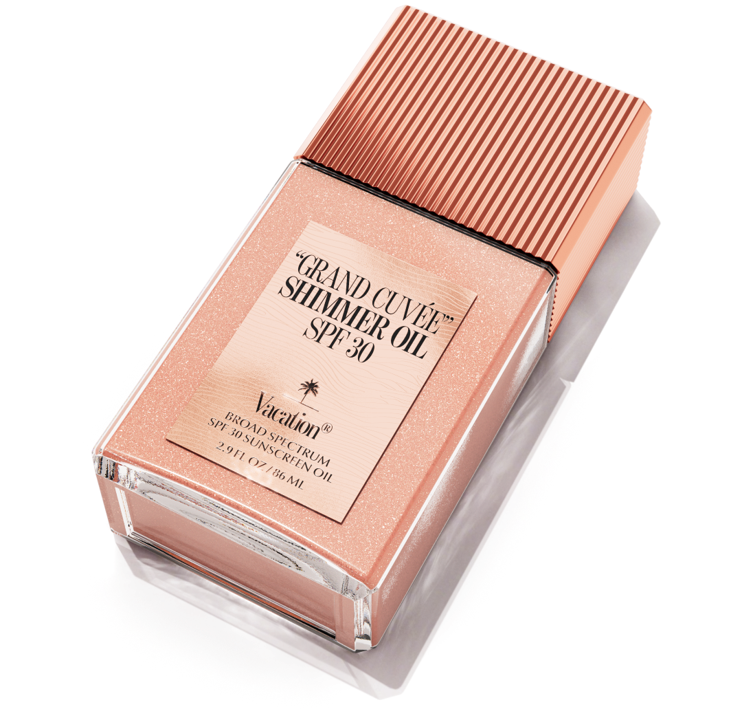 Vacation Grand Cuvée Shimmer Oil SPF 30 in a clear bottle with shimmery rosy-gold liquid and a matching ribbed cap.