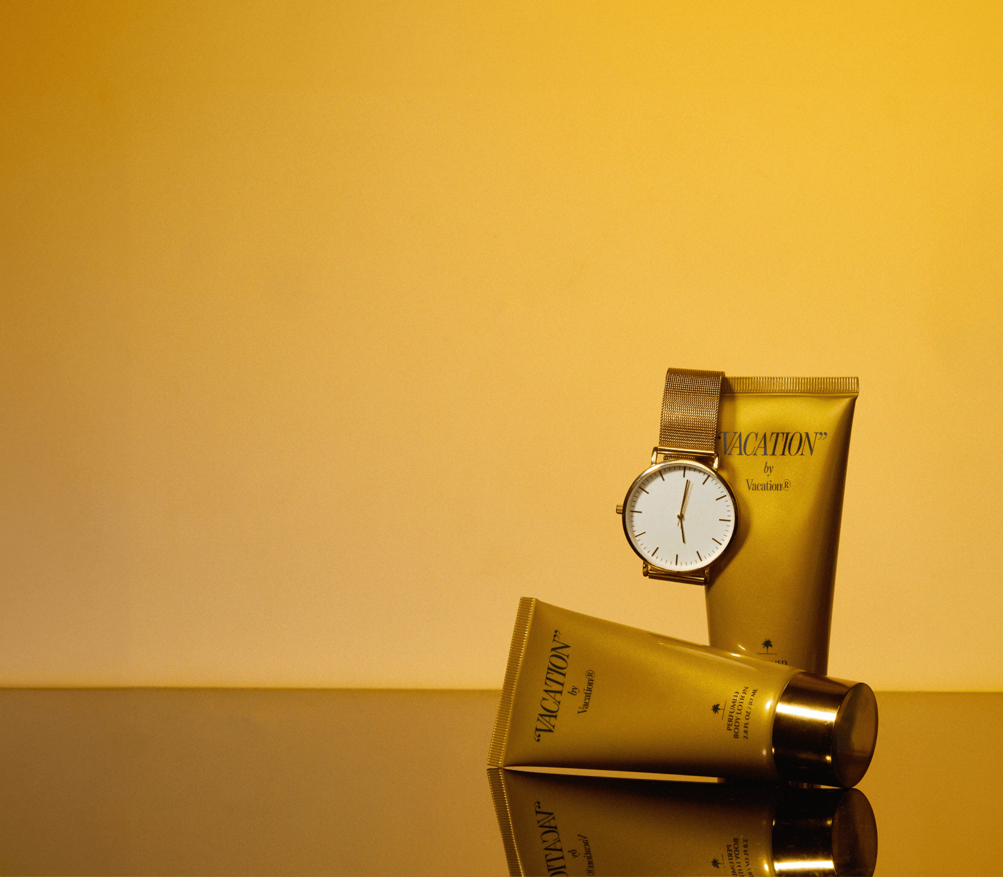 two tubes of "VACATION" by Vacation® on gold with a gold watch