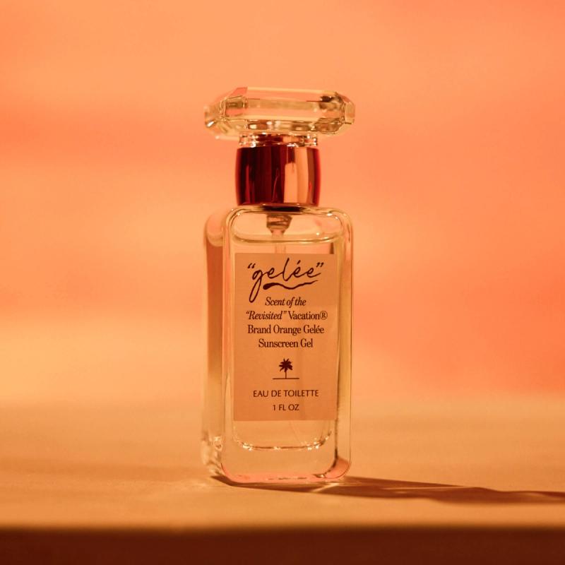 A clear glass bottle of "gelée" Eau de Toilette, described as the scent of orange gelée sunscreen, on an orange background.