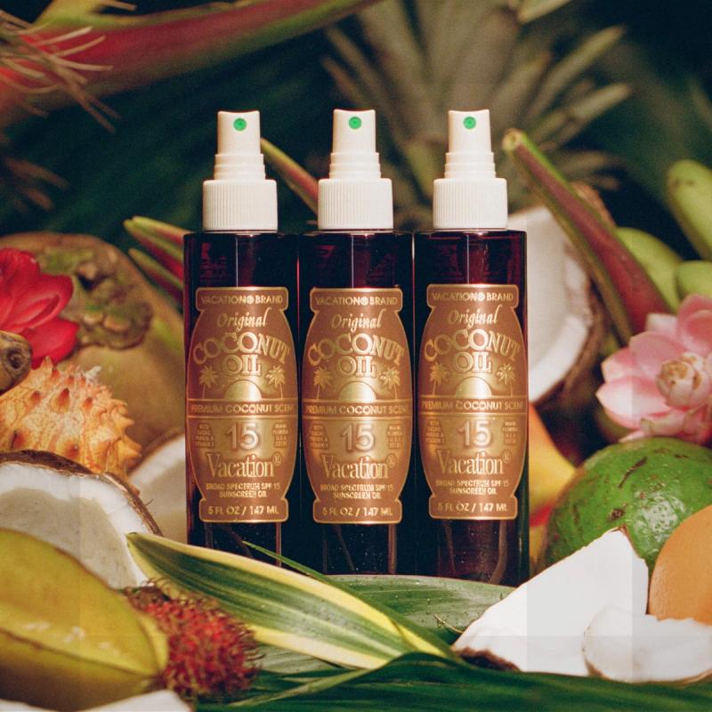 Three bottles of Vacation Brand Original Coconut Oil SPF 15 sunscreen amidst tropical fruits and foliage.