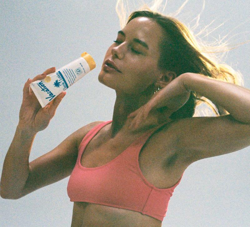 a woman in a pink bikini top is holding a bottle of sunscreen .