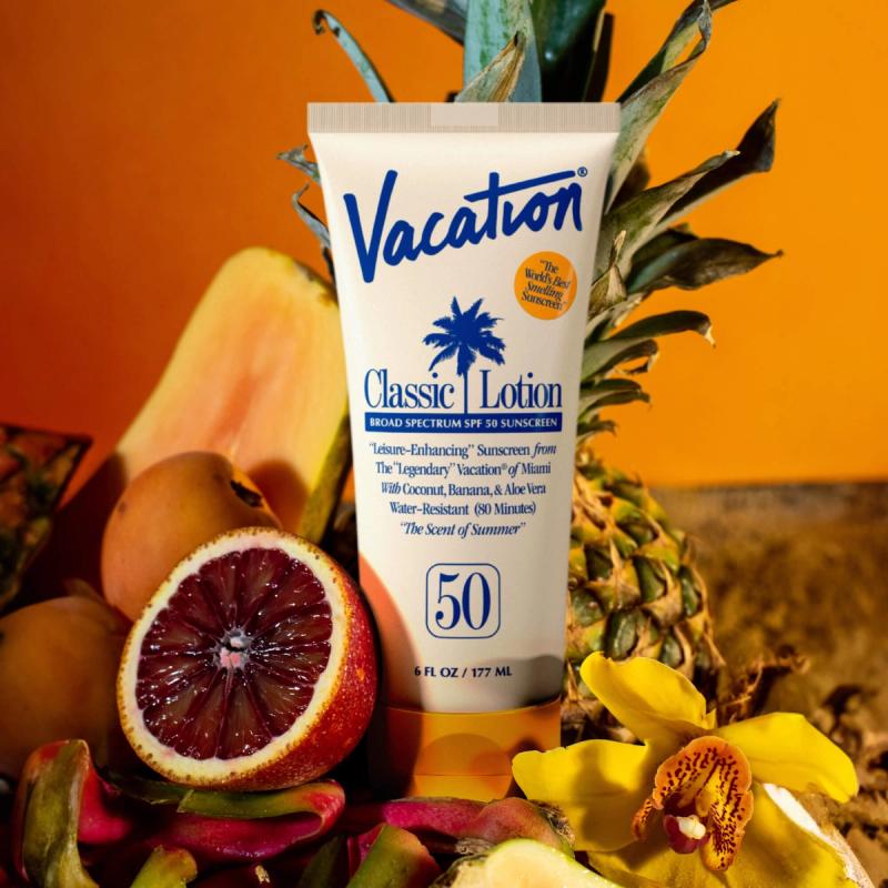 Vacation Classic Lotion SPF 50 sunscreen tube surrounded by tropical fruits and a yellow orchid on an orange background.