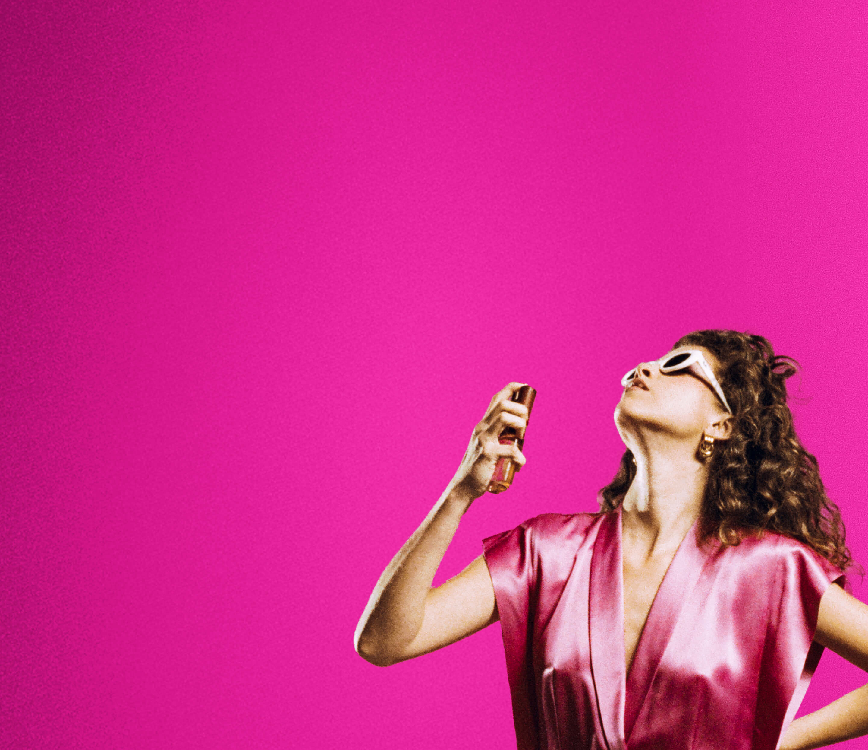 a woman in a silk pink jumper is spraying body mist