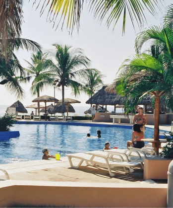 people are swimming in a large pool surrounded by palm trees