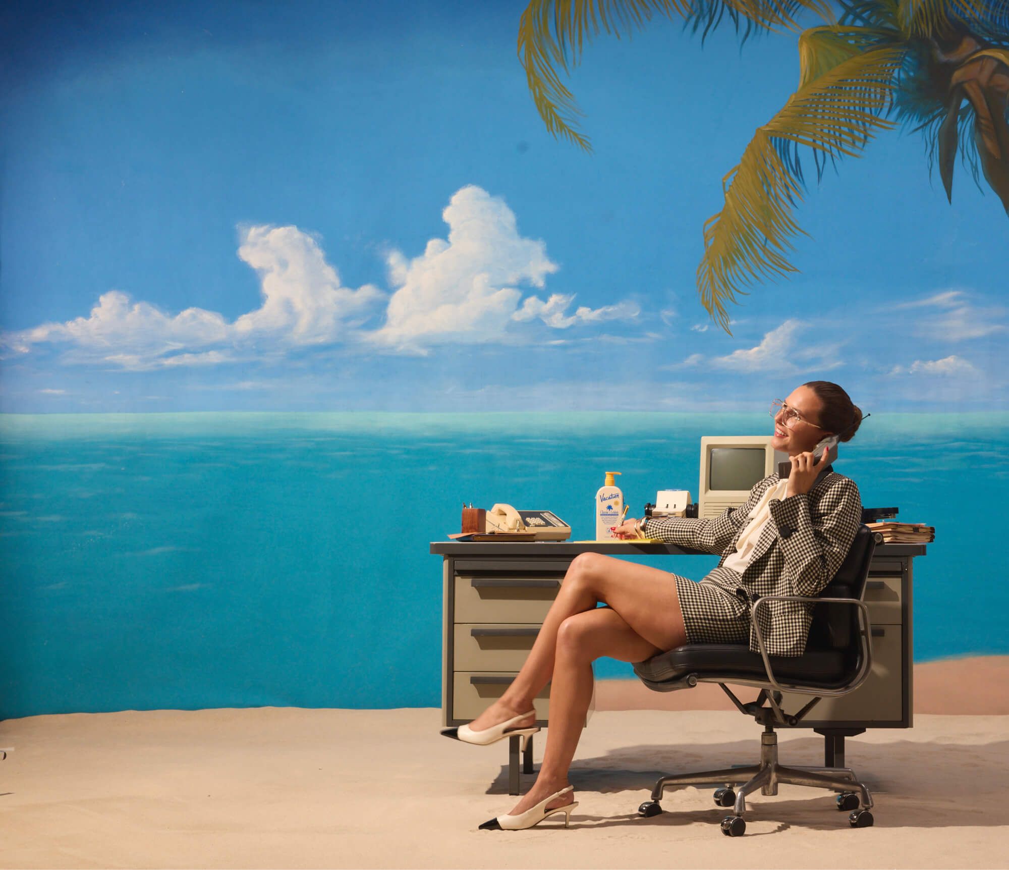 a woman sits at a desk on the beach talking on a cell phone