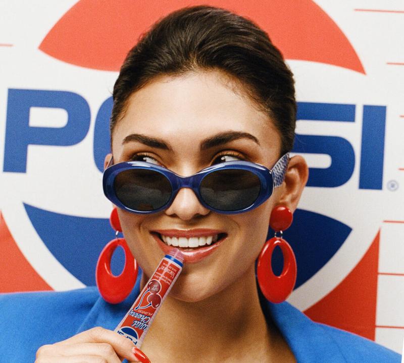 Three Vacation Pepsi Wild Cherry SPF 30 lip sunscreen tubes sit amidst shiny red cherries with blue stems.