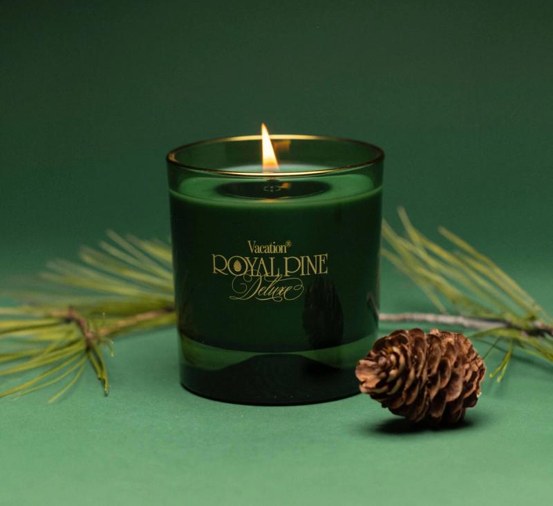 a green Royal Pine Deluxe candle on a green background with pine needles and pinecone