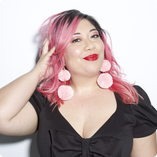 a woman with pink hair and pink pom pom earrings
