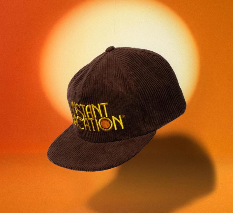 a baseball cap with the words `` instant vacation '' embroidered on it is sitting in front of a sun .