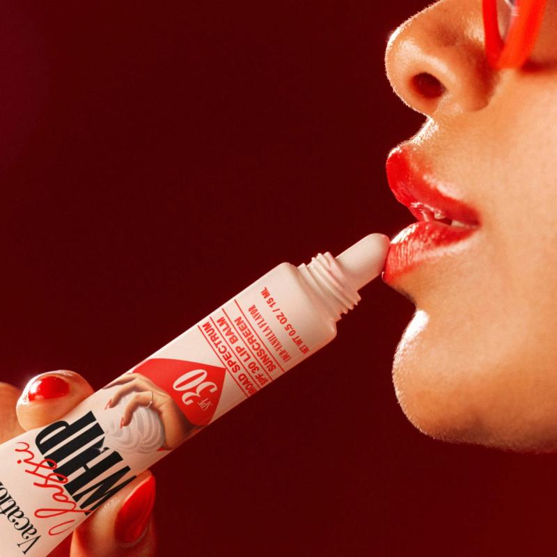 Close-up of a woman applying Vacation Classic Whip SPF 30 Lip Balm to bright red lips