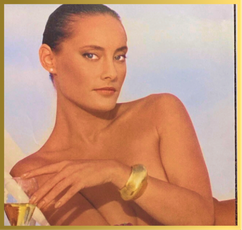 A tan-skinned woman with dark hair, bare shoulders, a pearl earring, and a golden cuff, looks directly at the viewer.