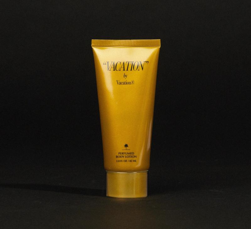 a gold tube of "VACATION" by Vacation® Perfumed Body Lotion on a black surface