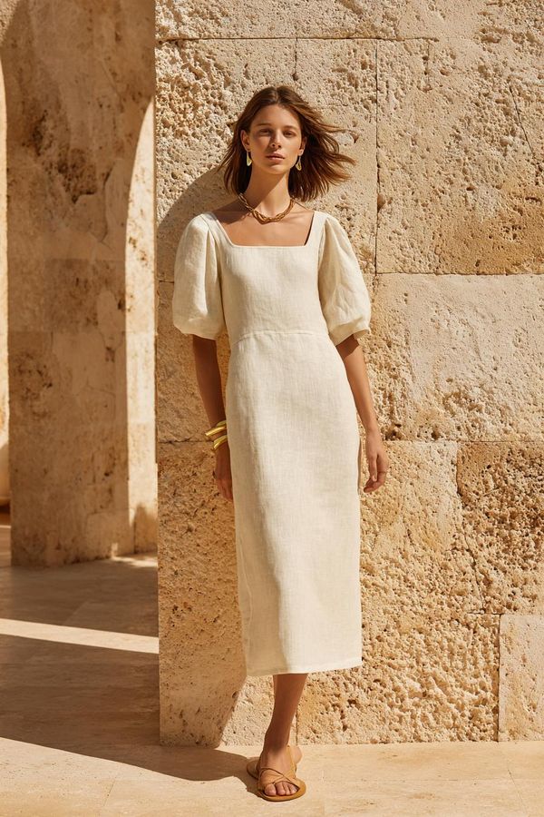 Sophisticated woman in cream linen midi dress with gold jewelry and leather sandals