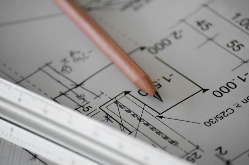 A pencil resting on a set of house plans, beside a ruler.