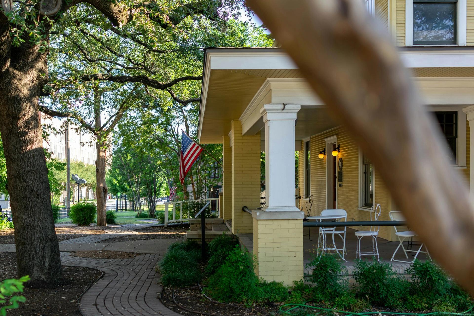 Yellow house with a porch, american flag, and brick pathway.