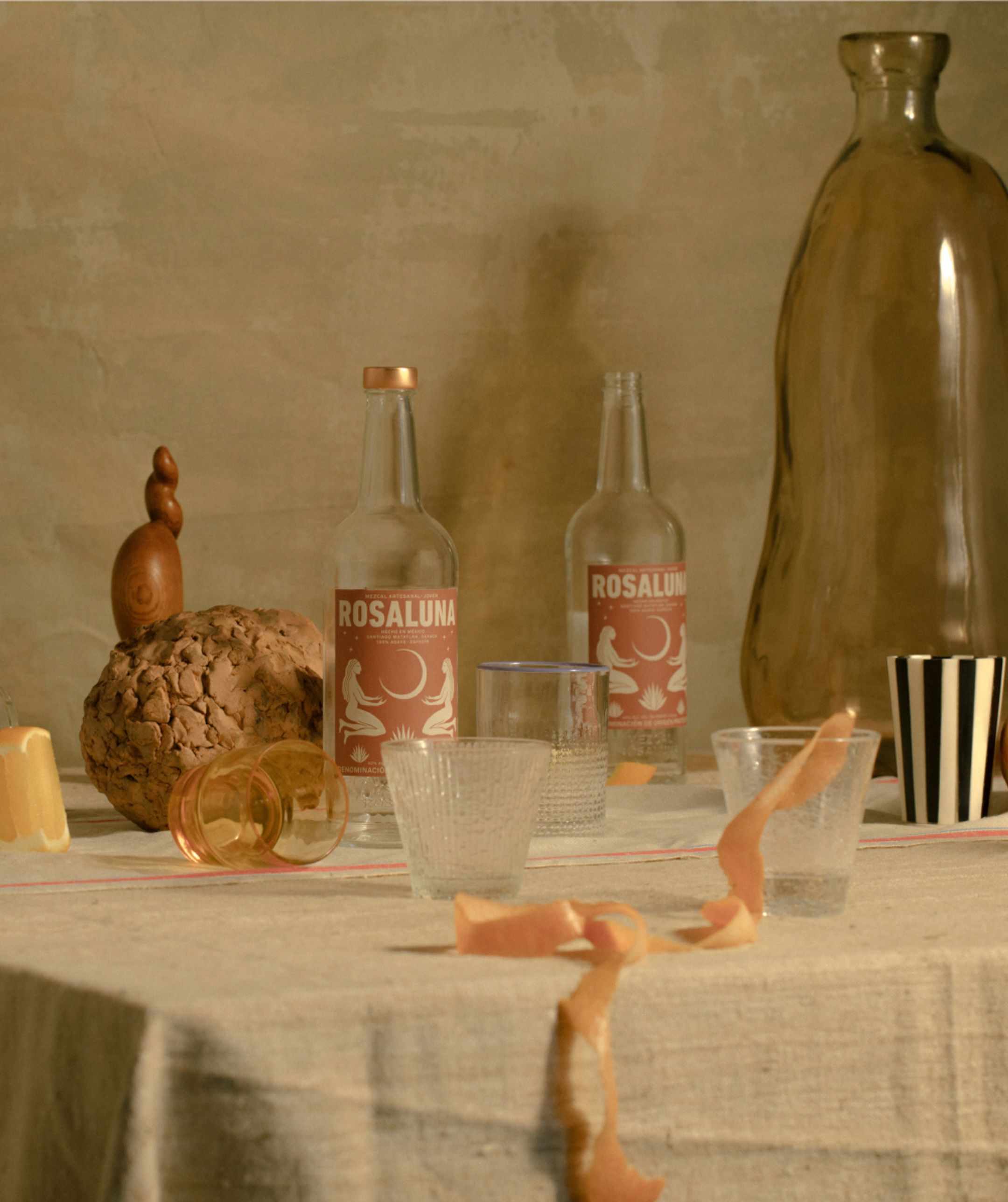 Still life of Rosaluna Mezcal bottles and assorted ceramics, fruit, and objects.