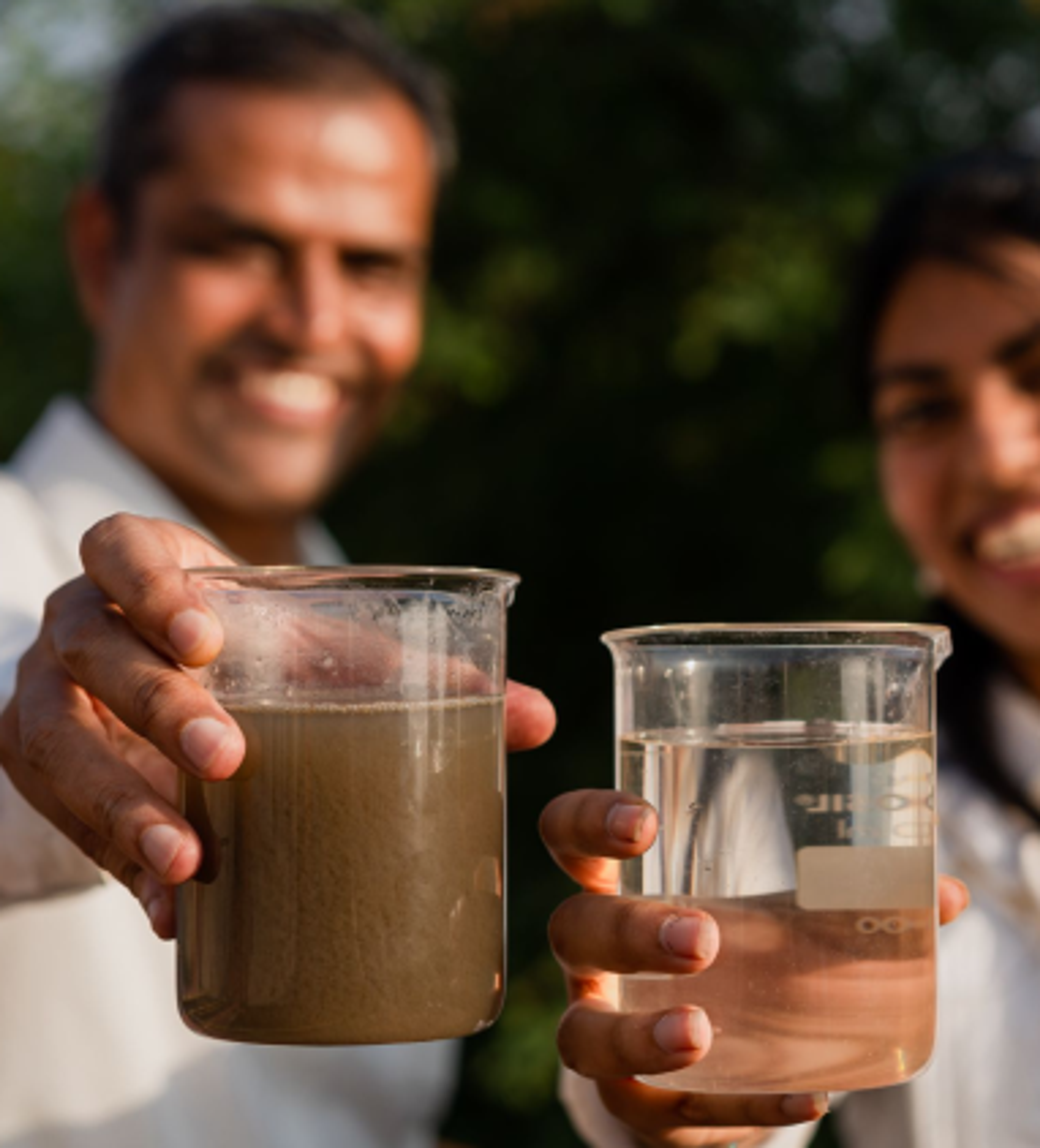 Two people holding laboratory cups filled with liquid. Copyright Cotton Design, Talia Cotton