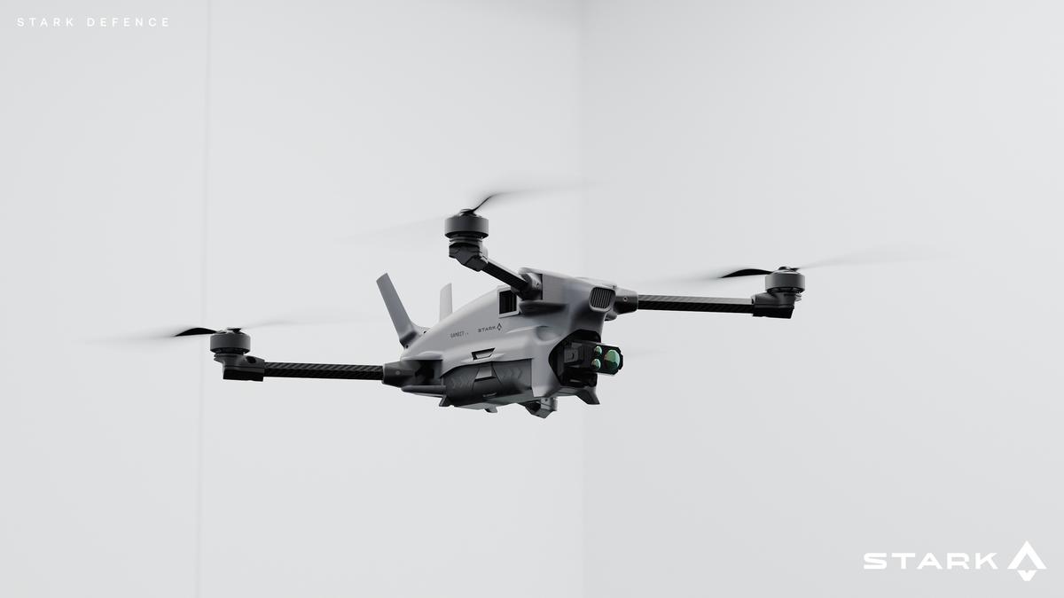 A grey drone with a camera attachment hovers against a white background, with "STARK DEFENCE" and "STARK" logos visible.