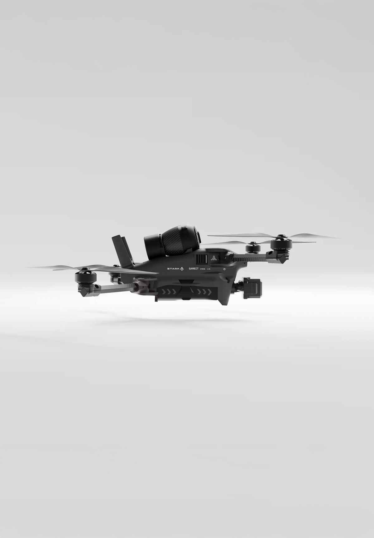 A dark gray quadcopter drone with a top-mounted spotlight and an underside camera, hovering against a plain light gray background.