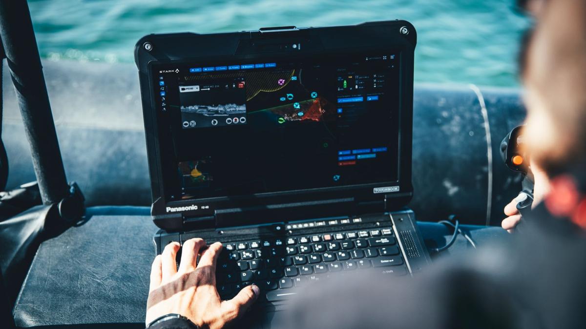 A person operates a rugged laptop on a boat, displaying a map and data interface on the screen.