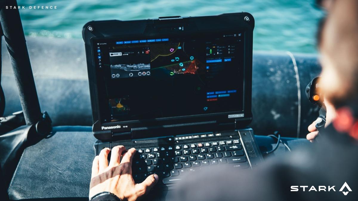 Person on a boat operating a rugged laptop displaying a navigation and surveillance interface for Stark Defence.