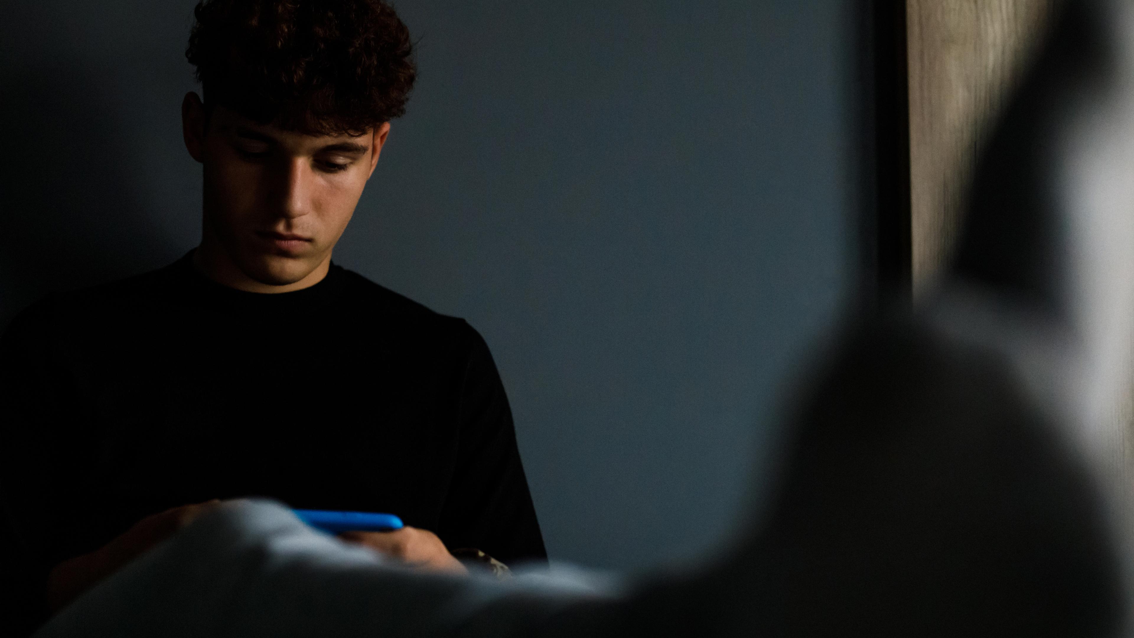 Dreng sidder i sin seng og kigger på sin mobiltelefon