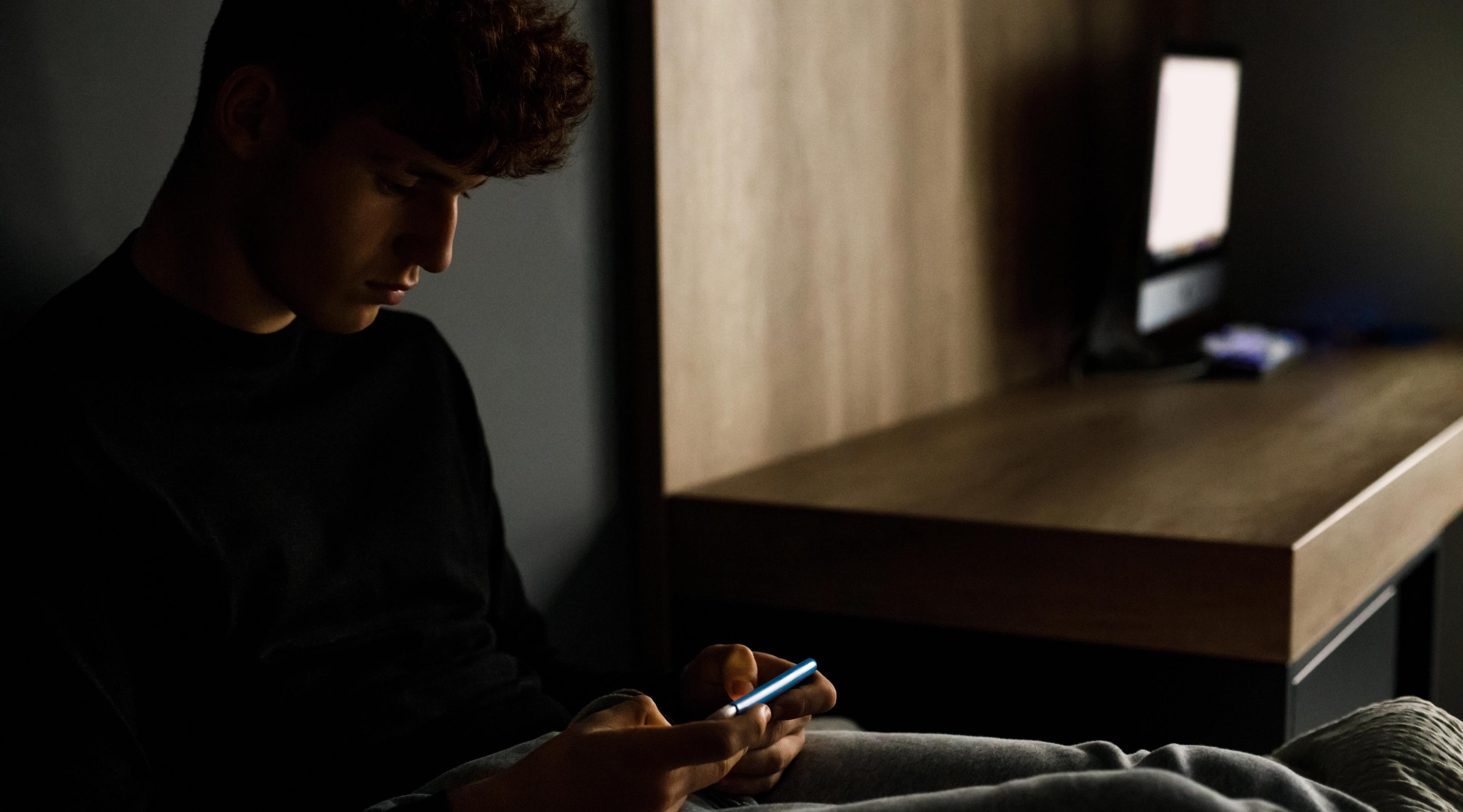 En dreng sidder med sin mobiltelefon.