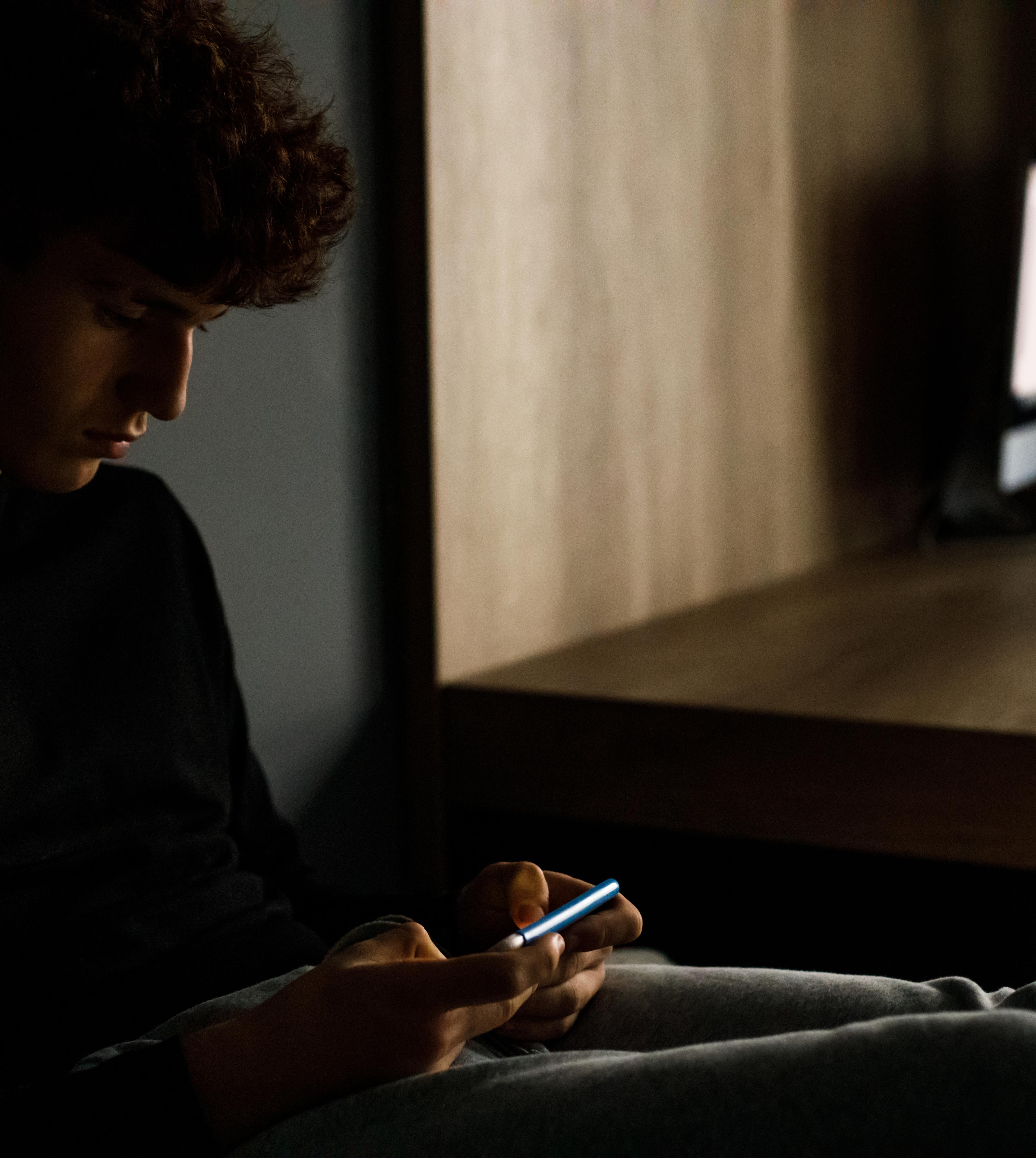 En dreng sidder med sin mobiltelefon.