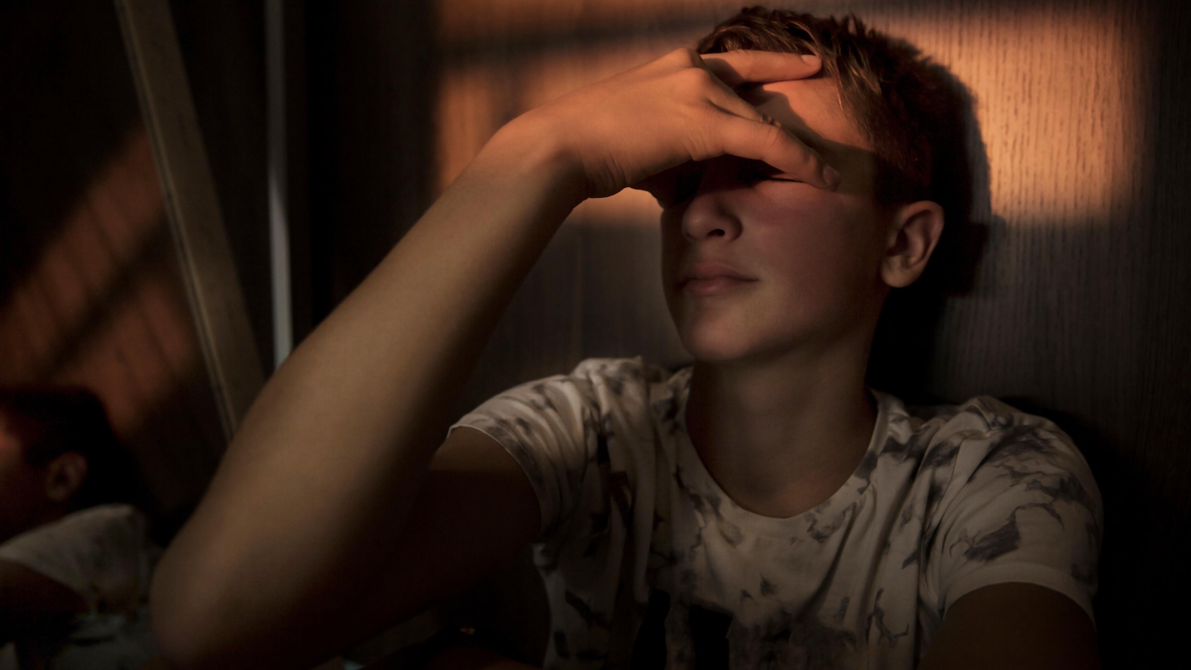 En dreng sidder i svagt sollys op ad en væg inden for. Han sidder med lukkede øjne og holder hånden op foran øjnene. Billedet skal forestille drengen, der er frustreret over sin ludomani.