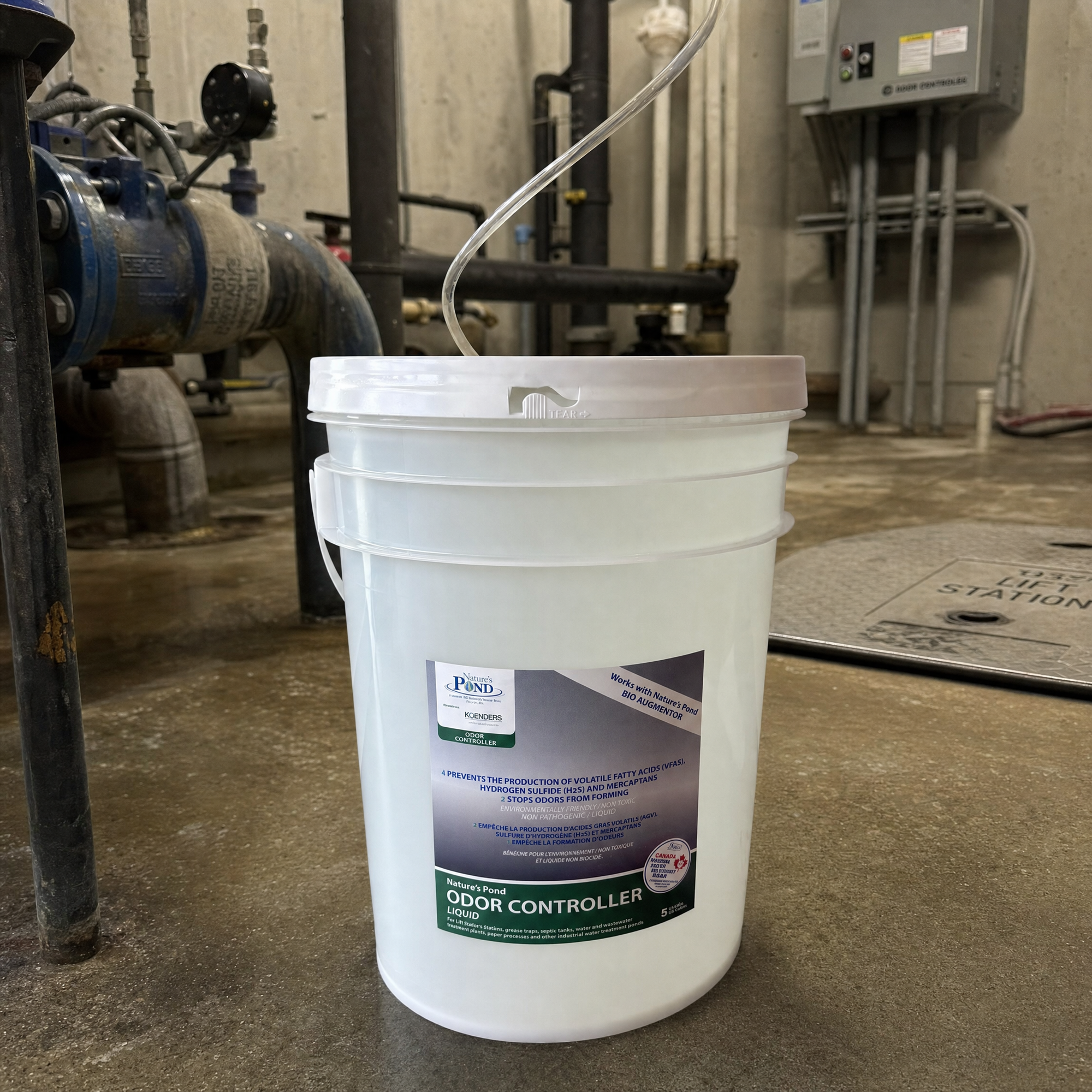 A sealed pail of Nature’s Pond concentrate beside a lift-station hatch, feeding the mixing unit through a draw tube