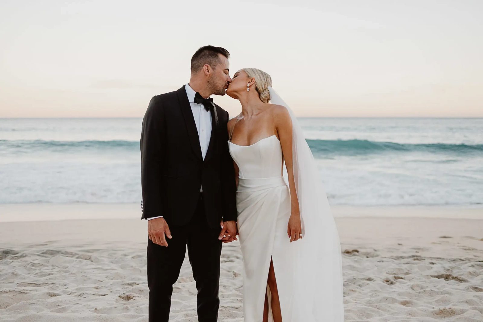 A MaidenWhite bride and groom kissing on the beach on their wedding day