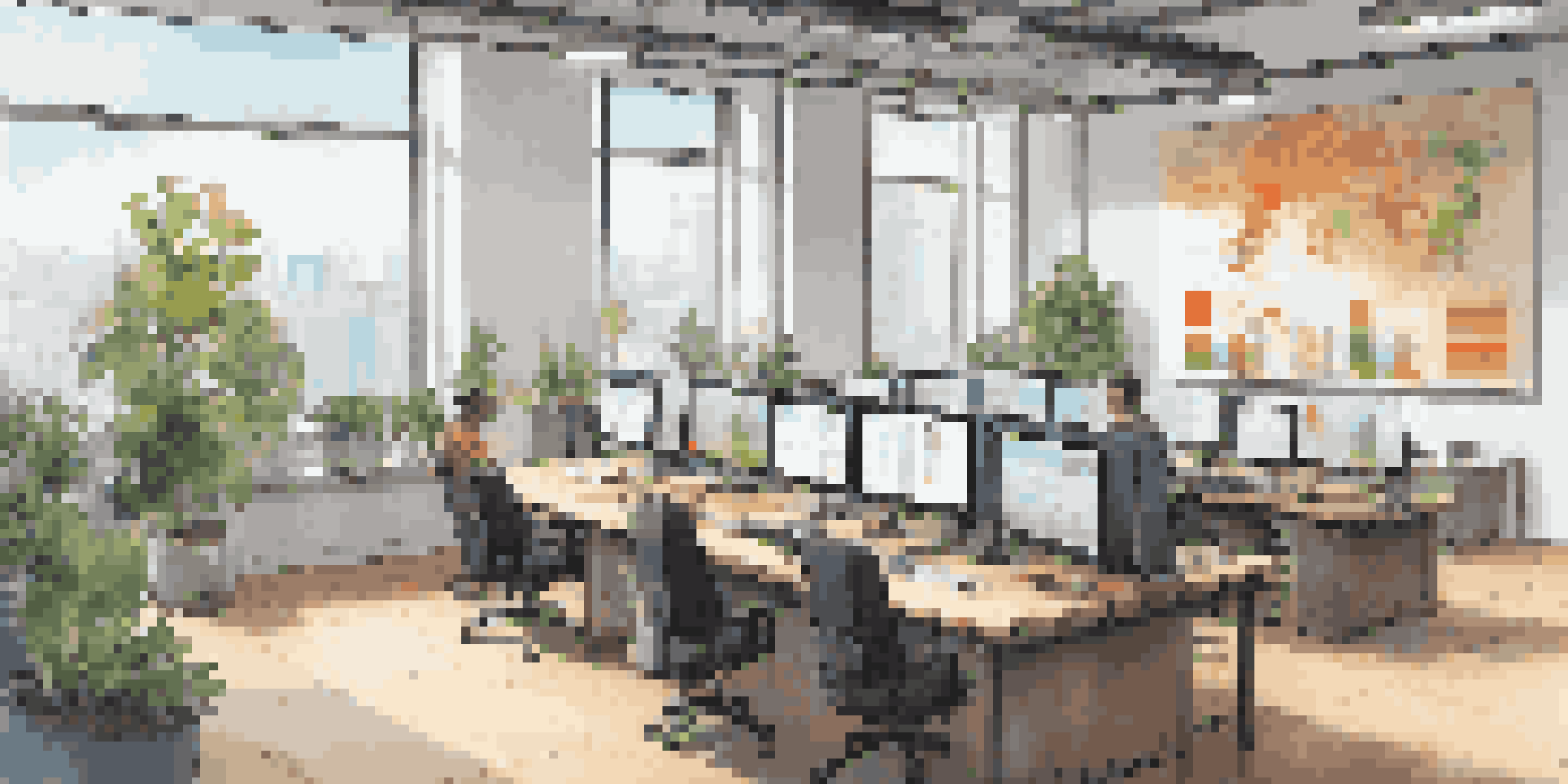 A bright and inviting modern office with a wooden table, laptops, plants, and a screen showing colorful data visuals.