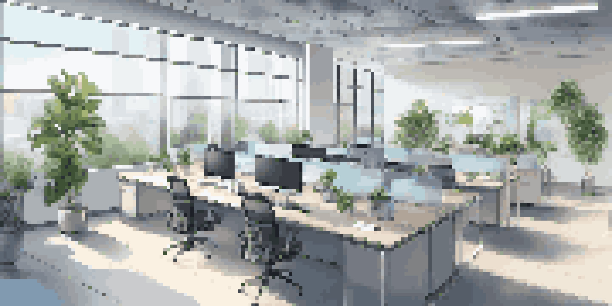 A modern office interior with computer workstations, a meeting area with glass walls, and indoor plants, all bathed in natural light.