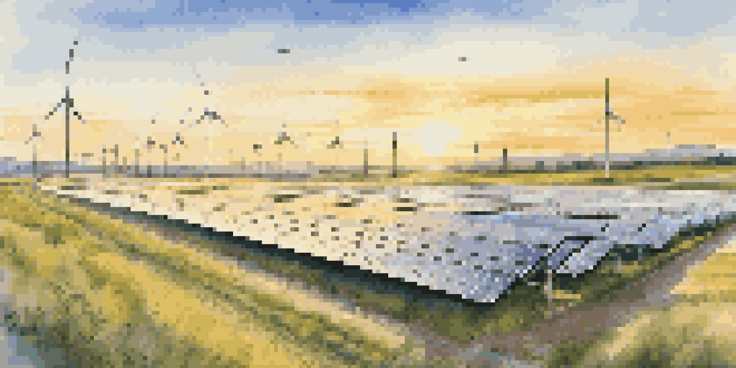 A sunrise view of a solar power farm with solar panels and wind turbines surrounded by green fields and wildflowers.