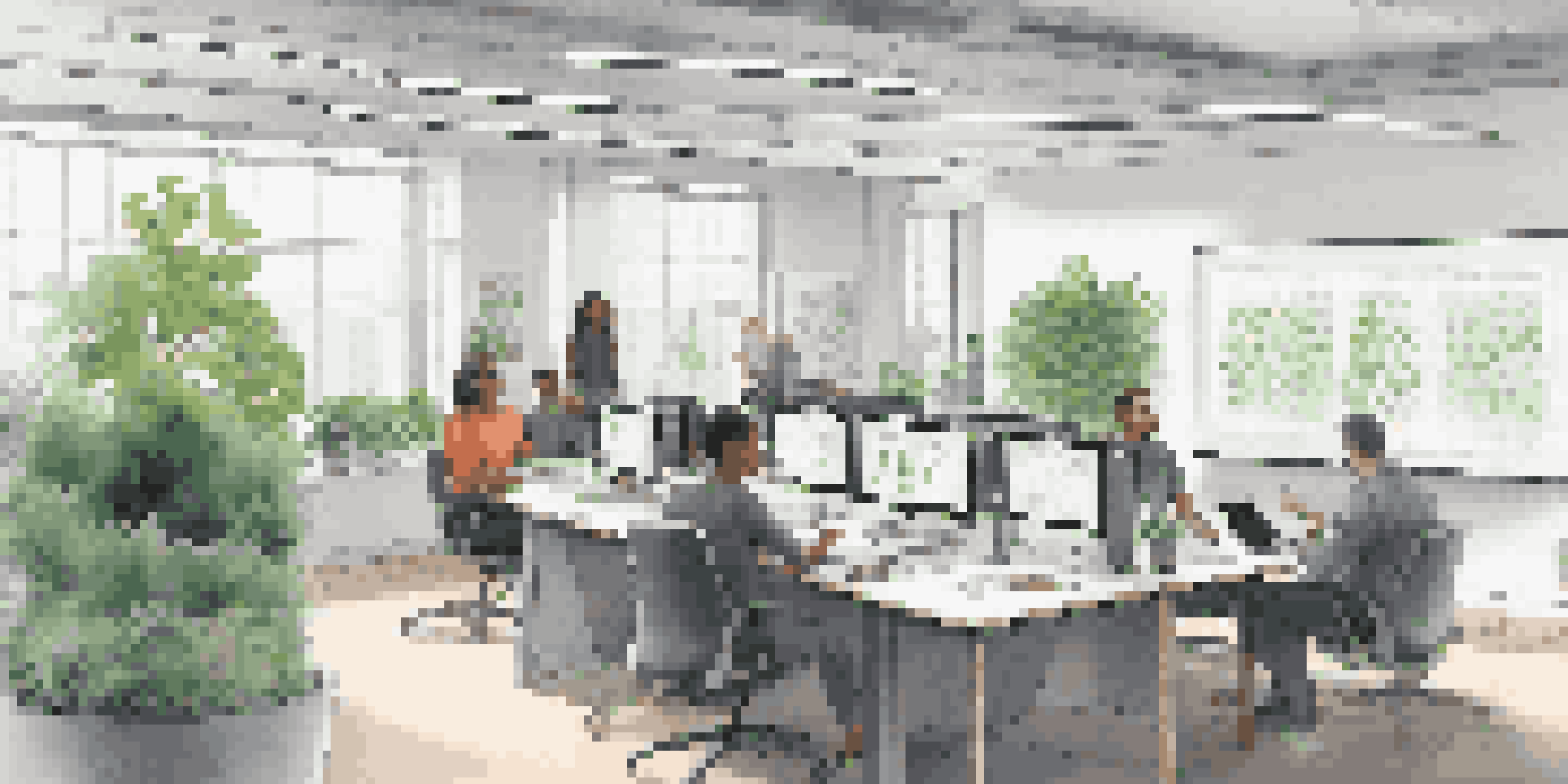 A diverse group of professionals engaged in discussion in a modern office, with a large table, whiteboard filled with diagrams, and plants in the background.
