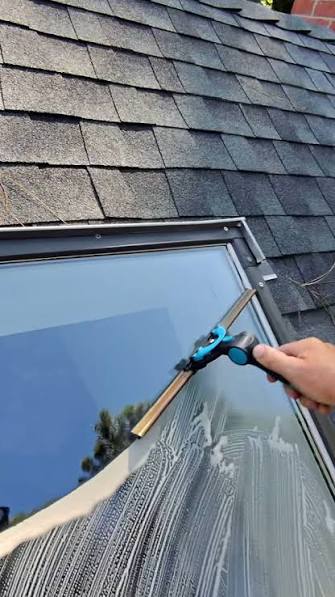 Technician squeegeeing a residential roof skylight during an exterior cleaning service