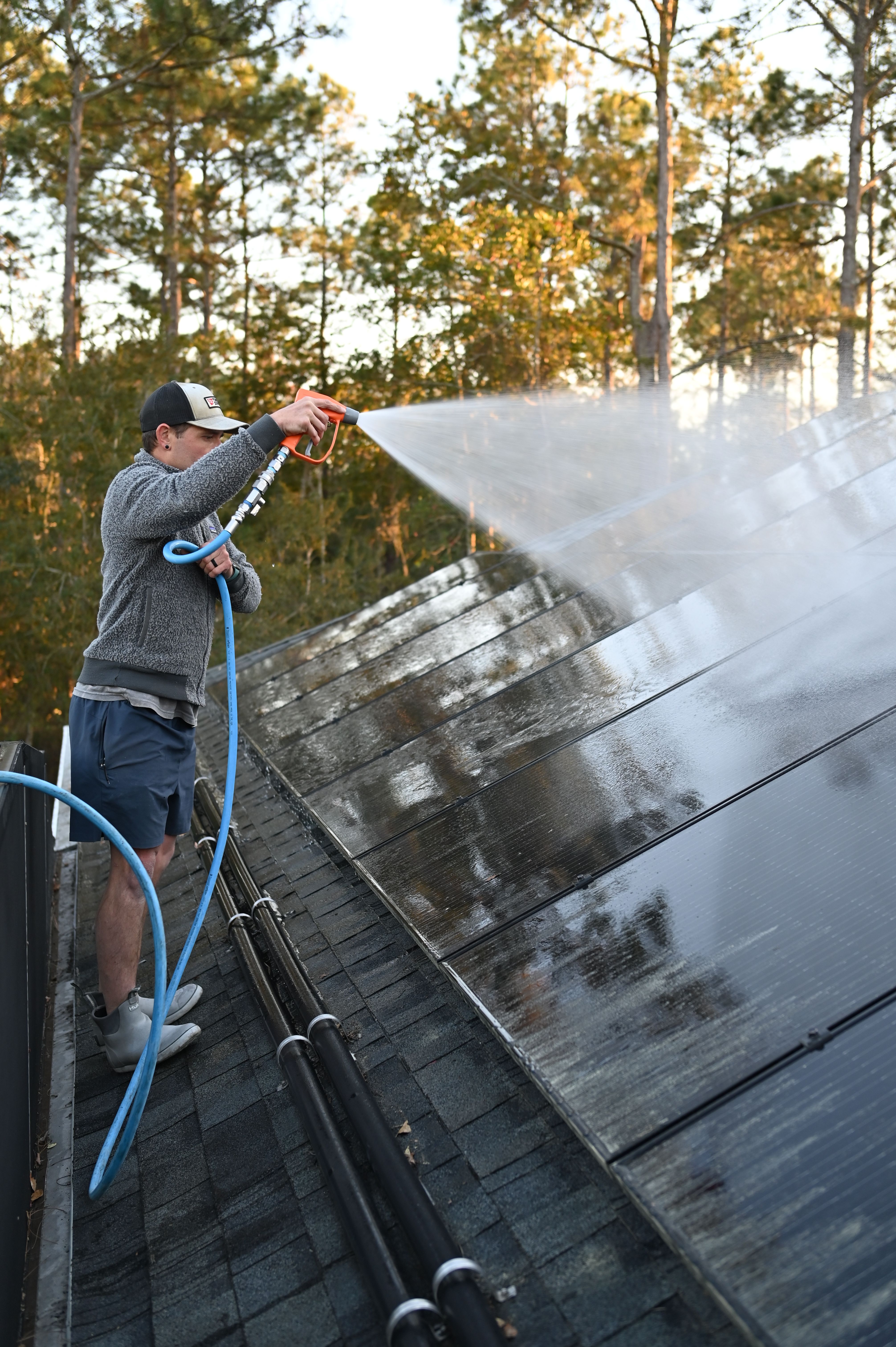 Technician rinsing a residential rooftop solar panel array with a soft wash hose at golden hour in St. Augustine, FL