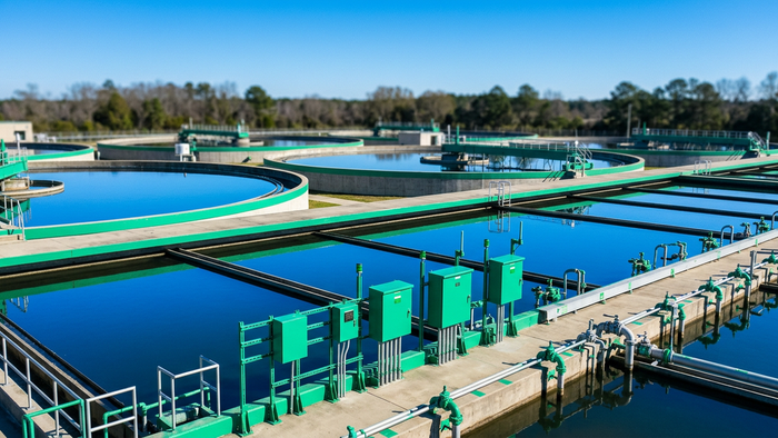 Wide shot of an outdoor water treatment facility with tanks, basins, and digital monitoring equipment cabinets under a clear sky
