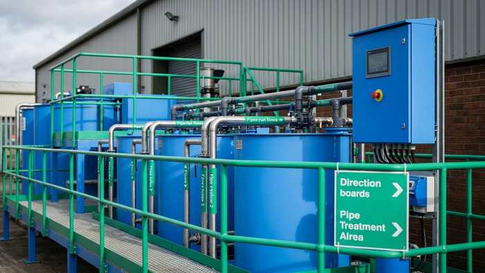 Editorial photograph of a compact SME-scale effluent treatment plant exterior with visible tanks, piping, and control panel in natural daylight