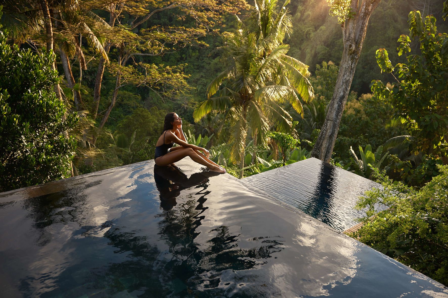 A guest relaxes in a jungle-edge infinity pool at golden hour