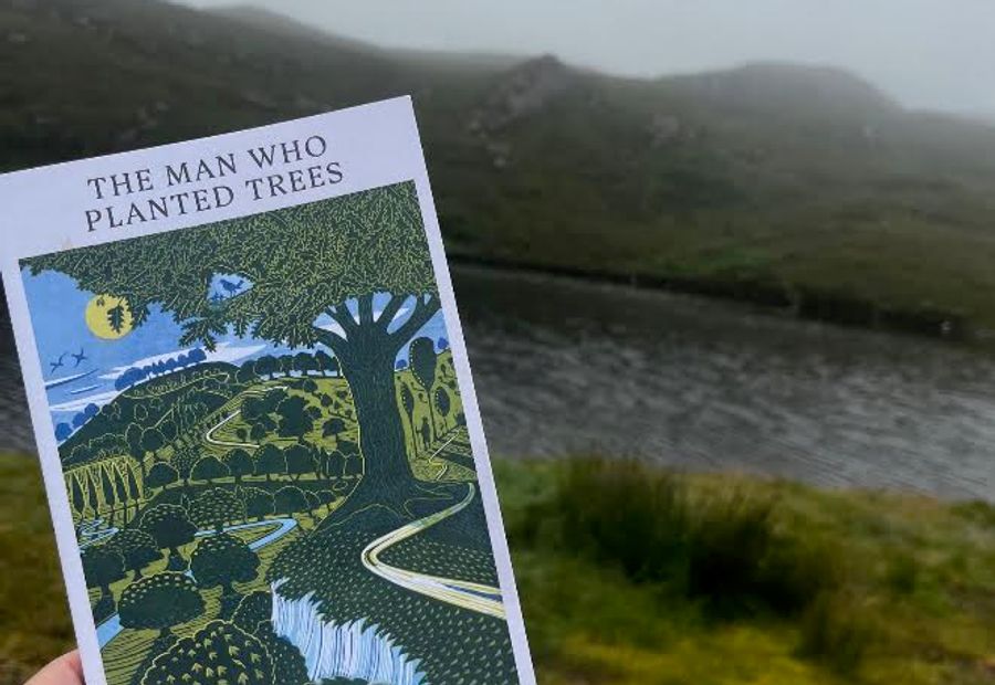 The book, The Man Who Planted Trees, held up against the backdrop of the North West Highlands of Scotland 