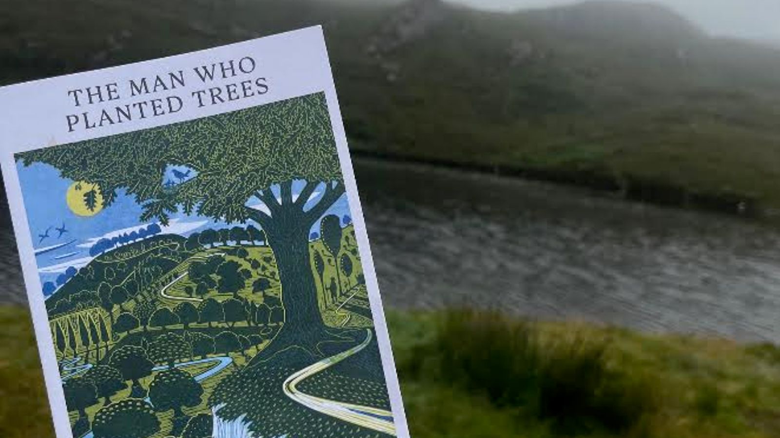 The book, The Man Who Planted Trees, held up against the backdrop of the North West Highlands of Scotland