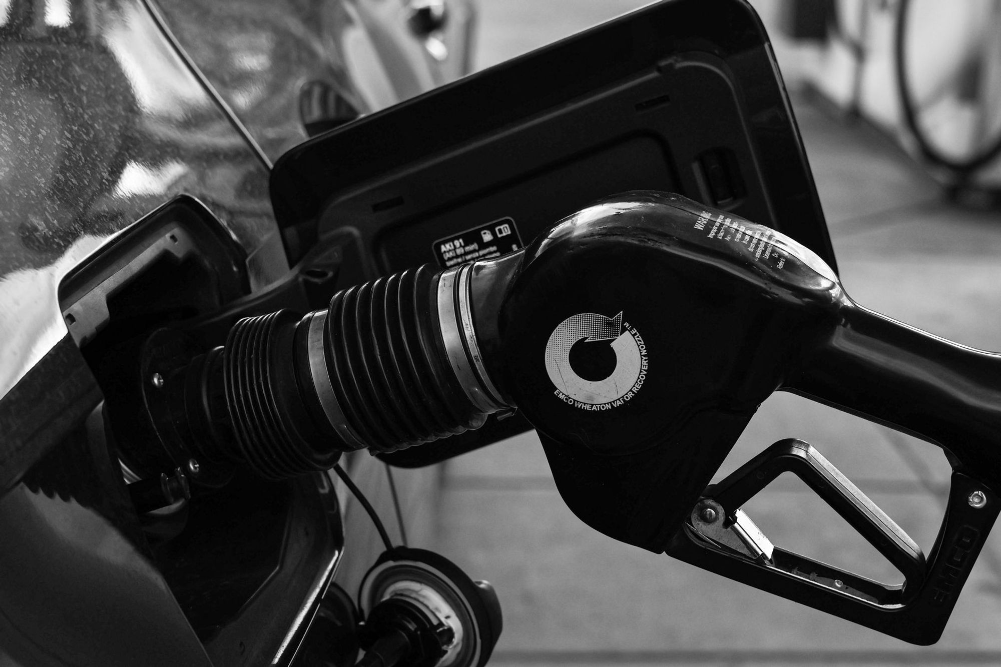 Black and white close-up of a fuel pump nozzle in a car's open fuel filler