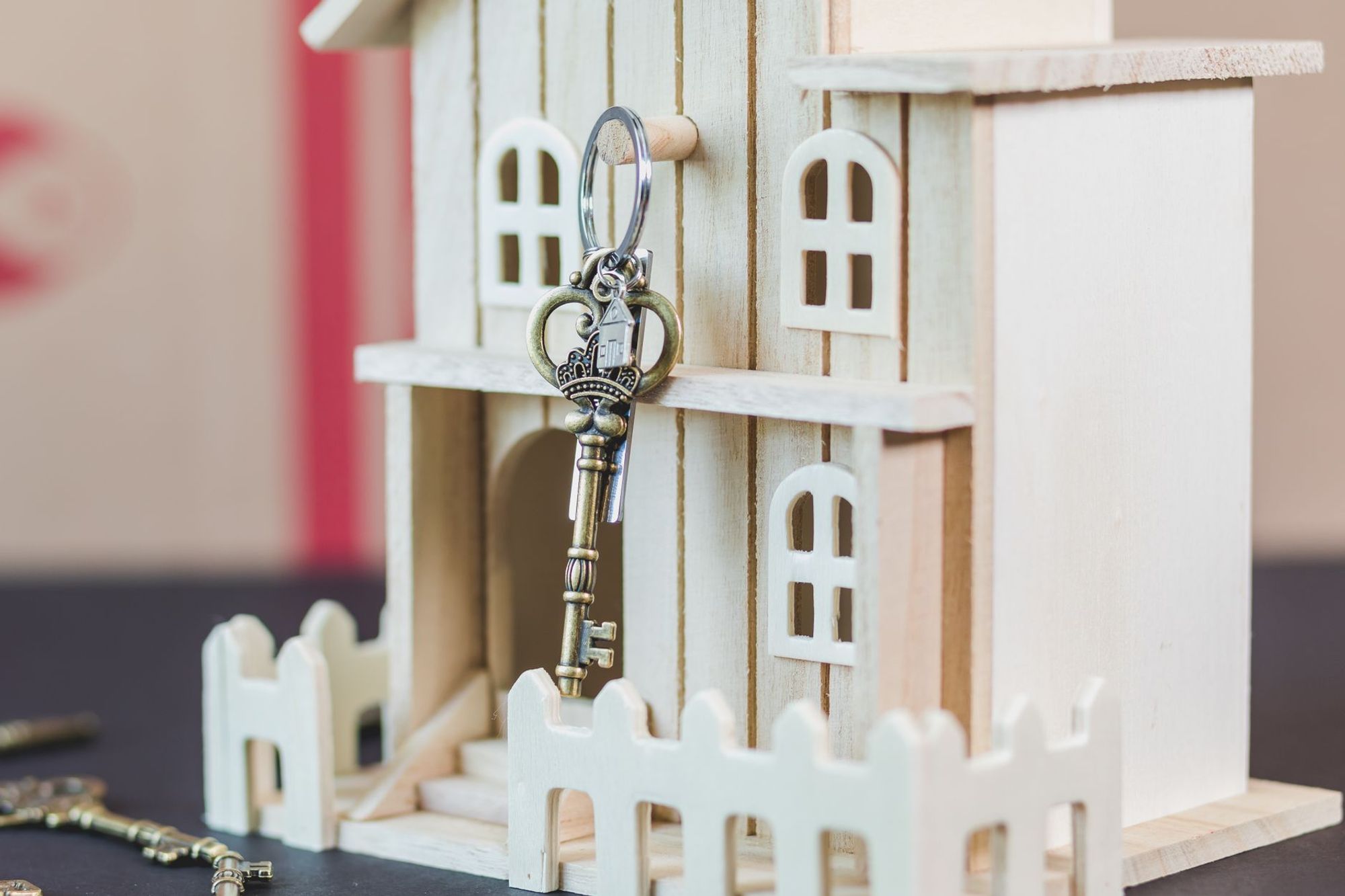 Vintage-style key hanging on a small white wooden model house behind a picket fence