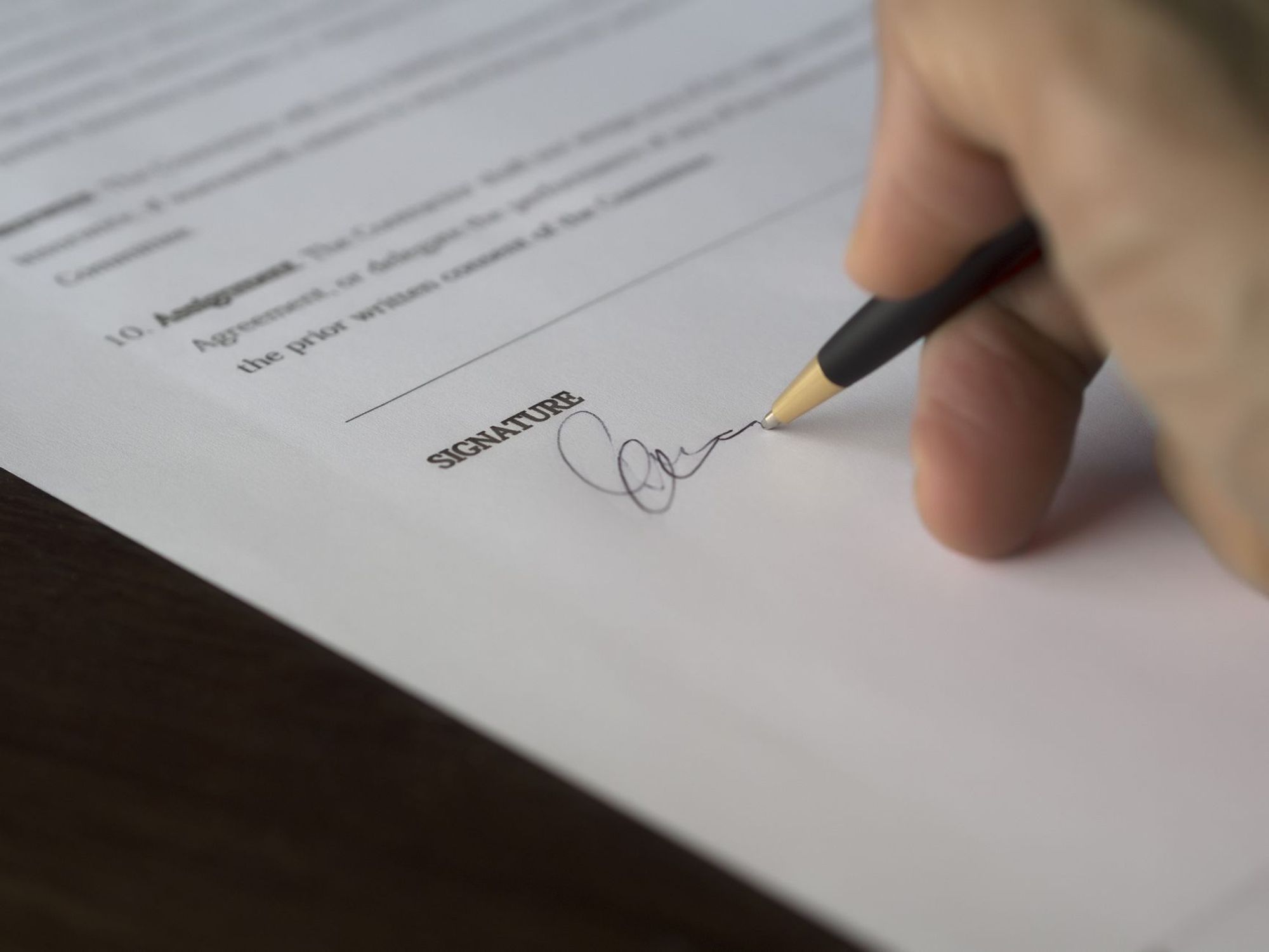 Close-up of a hand signing the signature line of a printed contract with a pen