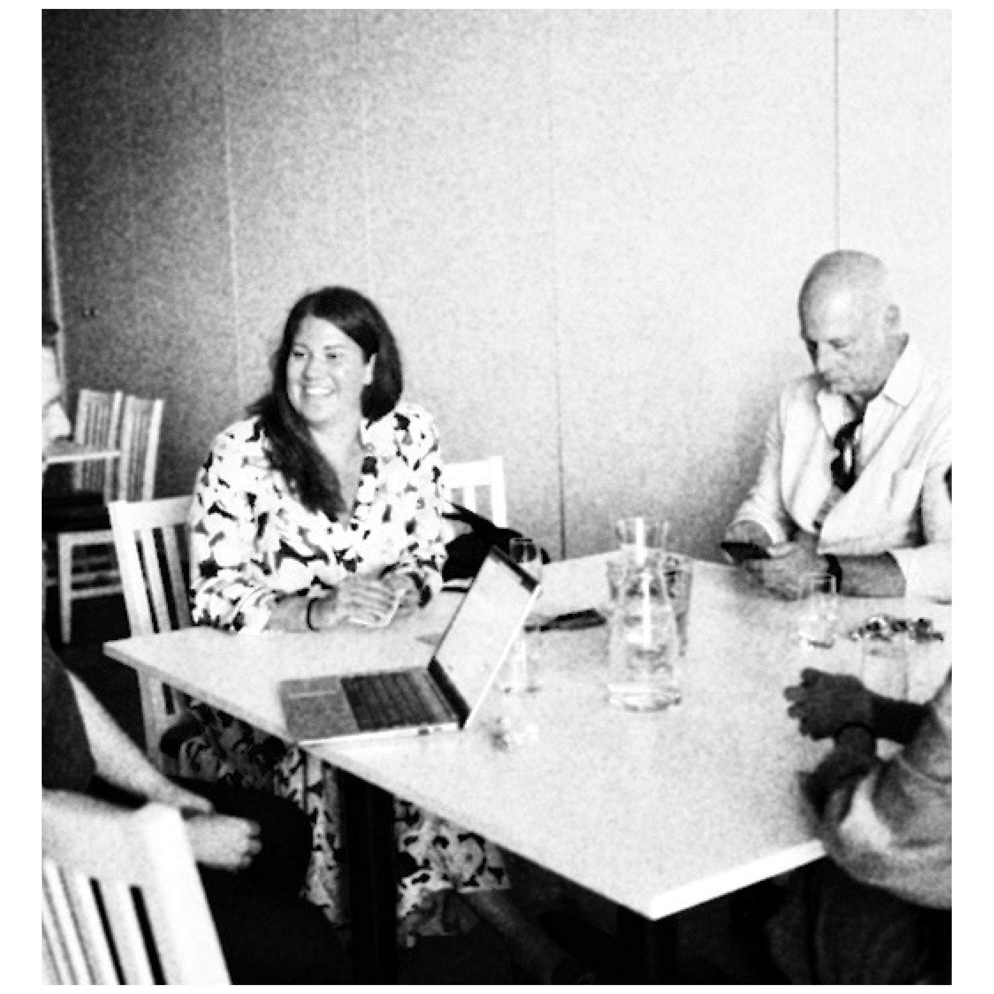 Syntolkning: ögonblicksfotografi från hackathon. I bild syns fyra personer, samtalandes runt ett konferensbord. PÅ bordet står dator, karaff, glas och anteckningsblock. Stämningen är koncentrerad och lättsam.