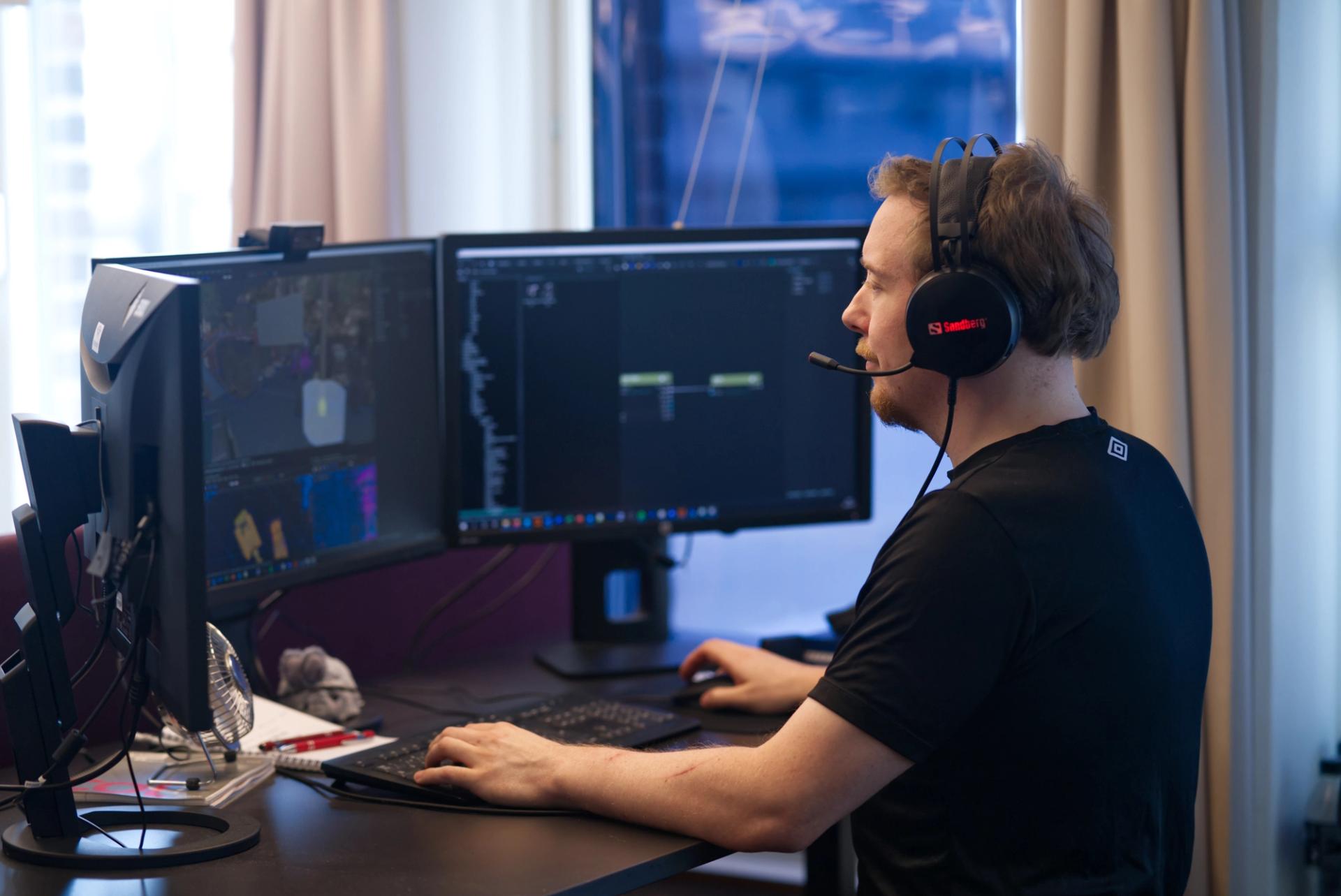 Employee with headset on standing at three screened computer setup, using different game development software